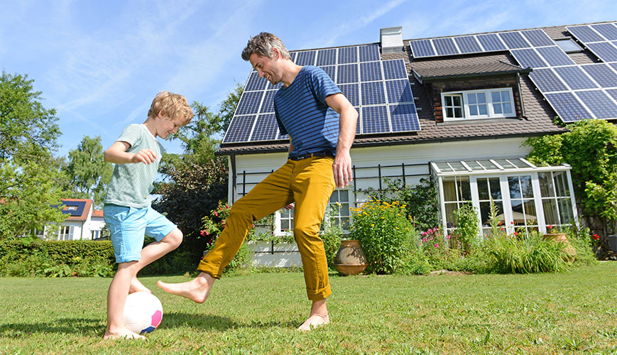 Vader en zoon voetballen in tuin bij huis met zonnepanelen