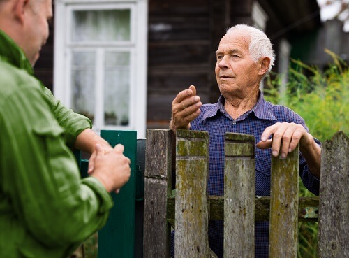 2 buurmannen praten met elkaar bij de schutting