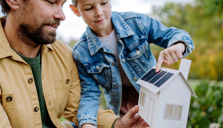 Vader en dochter kijken naar een maquette van hun huis met daarop miniatuurversies van de nieuwe zonnepanelen