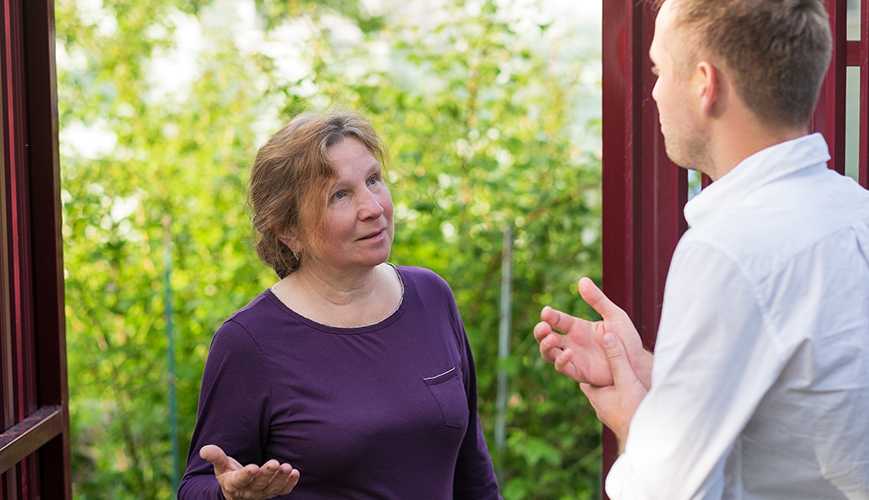 Een buurvrouw en buurman discussiëren bij een poort. 